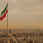 Iranian flag waving over a city skyline with mountains in the background