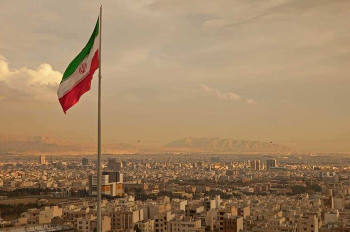Iranian flag waving over a city skyline with mountains in the background