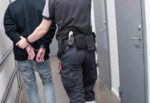 Officer escorting handcuffed person down hallway.