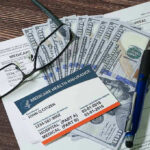 Stunning Hospice Scam – $600 Million Exposed! Medicare card glasses pen money on wooden table