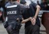 Police officer arrests handcuffed person.
