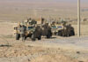 Soldiers beside military vehicles in a desert area.