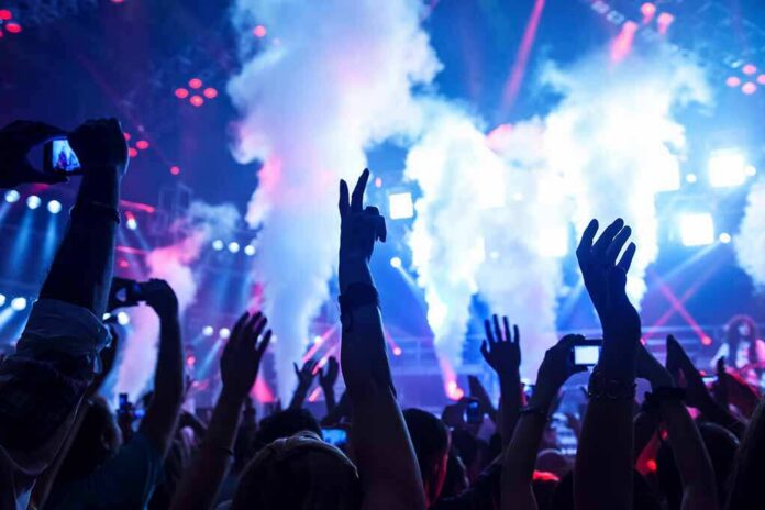 Picture,Of,Rock,Concert,,Music,Festival,,New,Year,Eve,Celebration, Crowd at a concert with hands raised and smoke effects in the background