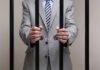 Surgeon’s Shocking Act: Forced Abortion Pills Businessman in a suit holding prison bars with handcuffs on his wrists