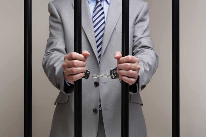 Businessman,Behind,Bars,In,Prison,Concept,For,White,Collar,Crime Businessman in a suit holding prison bars with handcuffs on his wrists