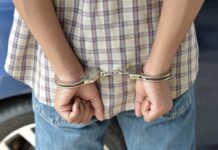 A person in handcuffs viewed from behind, wearing a plaid shirt and denim jeans