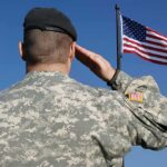 Soldier in military uniform saluting in front of an American flag