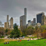 Motorcycle Mayhem In NYC Park City skyline with park and people relaxing.