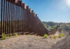 Border Wall Ultimatum Hits Texas Families Tall metal border wall with rural landscape.