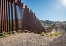 Border Wall Ultimatum Hits Texas Families Tall metal border wall with rural landscape.