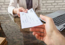 Donor Money Wired To Extremists? Hands exchanging a check near a laptop.