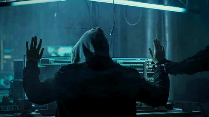 680075263 Hacker in hoodie arrested at computer desk.