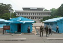 Strait Reopens, Bomb Clock Ticks Military personnel standing near blue buildings at a border crossing