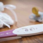 A pregnancy test next to a pacifier and a knitted baby hat on a wooden surface