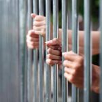 Murderers on ‘Early Release’ List? Hands gripping metal prison bars