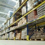 Factory Boom Hype Masks Risky Stockpiles Interior view of a warehouse with stacked shelves of packaged goods