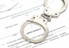 Inside Job: 100 Detroit Homes Vanish Handcuffs on top of an arrest warrant document.