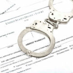 Inside Job: 100 Detroit Homes Vanish Handcuffs on top of an arrest warrant document.