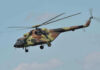 Black Hawks Swarm Camp—Why? Camouflage military helicopter in flight against blue sky.