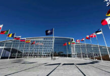 NATO Showdown: Trump Demands Greenland Flags outside NATO headquarters building under clear blue sky.