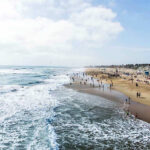 Blue Angels Flyby Sparks Navy Probe Crowded beach with waves and people enjoying sun.