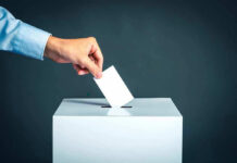 Hand placing ballot into voting box.
