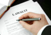 Hand holding pen, filling out lawsuit form.