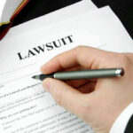 Hand holding pen, filling out lawsuit form.