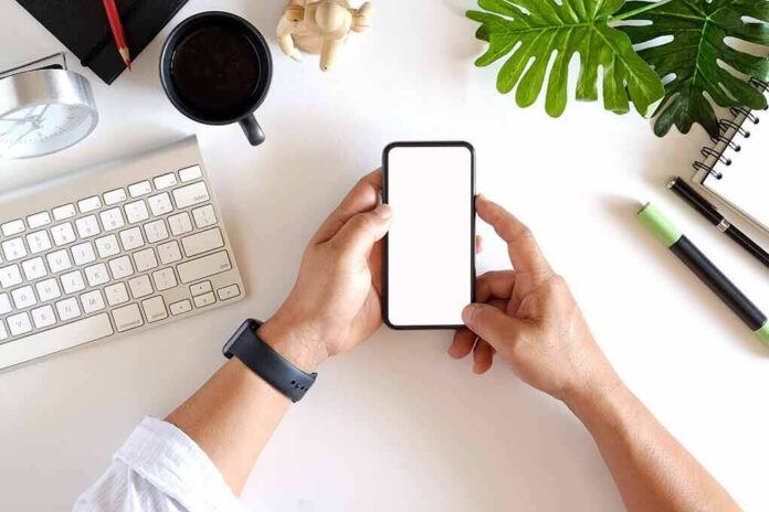 shutterstock_1020407980 hands holding smartphone over tidy desk