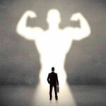 Businessman with briefcase casts a large muscular shadow on wall