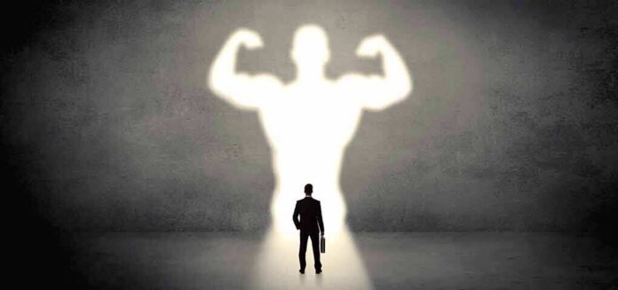Businessman with briefcase casts a large muscular shadow on wall