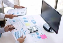 Mass Shooting Math: Pick a Side Business hands reviewing charts with a calculator and monitor on desk