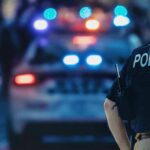 Flock Cameras Turned Into Stalker Tool police officer in vest near patrol car with flashing lights