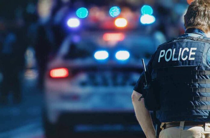 shutterstock_1543591088 police officer in vest near patrol car with flashing lights