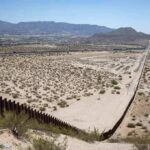 Border fence cutting across a desert landscape with mountains in the distance