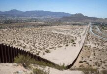 Border Wall Drilling STOPS — Permits Ignored? Border fence cutting across a desert landscape with mountains in the distance