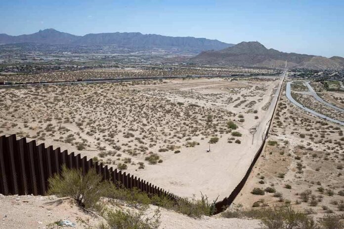 shutterstock_2006817503 Border fence cutting across a desert landscape with mountains in the distance