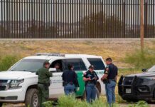 Fake Troops Run Border—Officials Stunned law enforcement officers confer beside patrol vehicles near a border fence