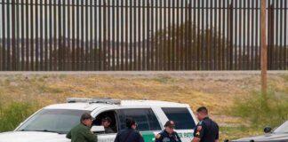 law enforcement officers confer beside patrol vehicles near a border fence