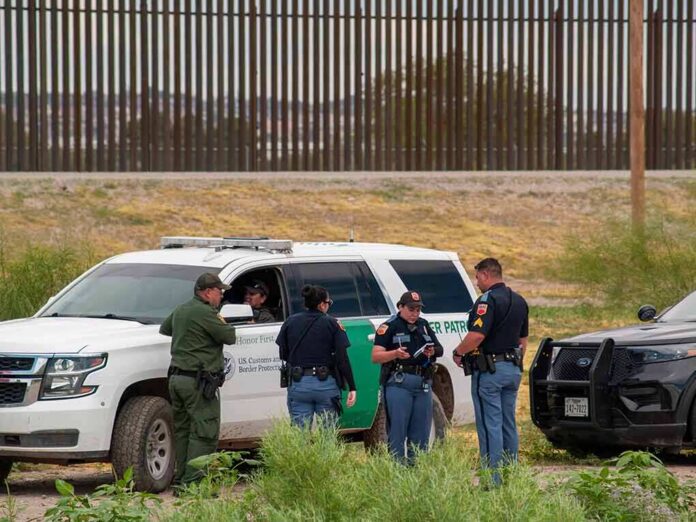 shutterstock_2015745392 law enforcement officers confer beside patrol vehicles near a border fence