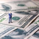 Miniature businessman standing on US dollar bills