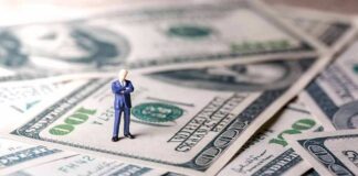 Miniature businessman standing on US dollar bills