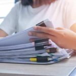 Teacher’s Double Life Explodes Online Person organizing a stack of documents with binder clips