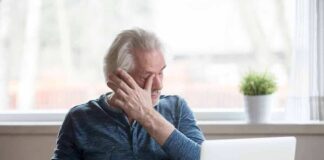 Older man rubbing his eye while sitting at a laptop