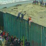 Border Meltdown Stuns Spain People climbing a tall beachside border fence