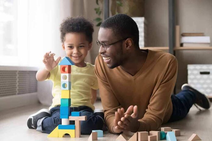 shutterstock_1319345771 Father and child building a tall tower with colorful wooden blocks on the floor
