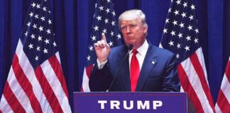 man in suit speaking at podium with multiple American flags