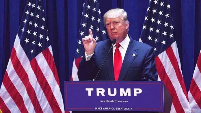 man in suit speaking at podium with multiple American flags