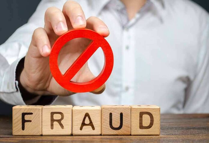 shutterstock_1488438023 Person holding red prohibition symbol over wooden blocks spelling fraud