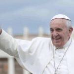 elderly man in white religious attire waving outdoors